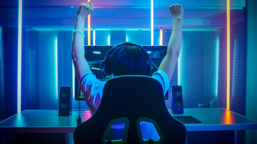 A gamer with his arms in the sky, celebrating victory, with RGB lighting all around his gaming setup.