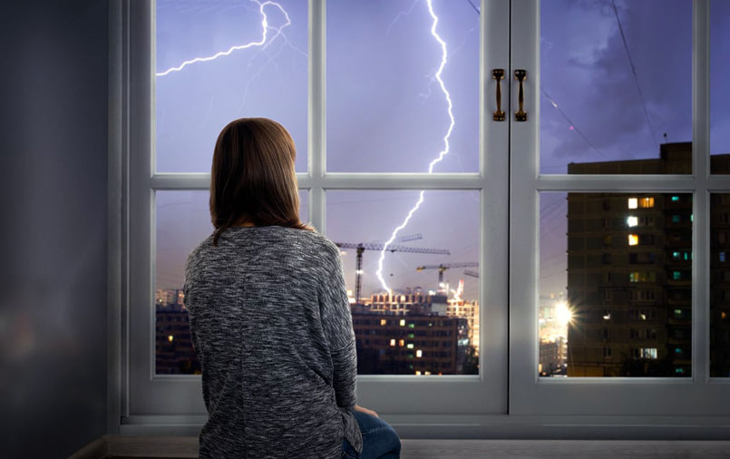 Girl watching lightning outside the window