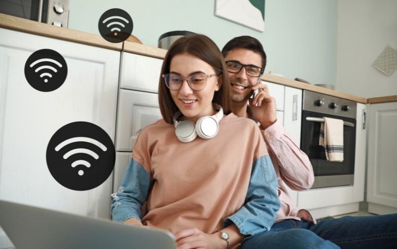 A couple sitting on the kitchen floor on the computer with wifi signals floating around them