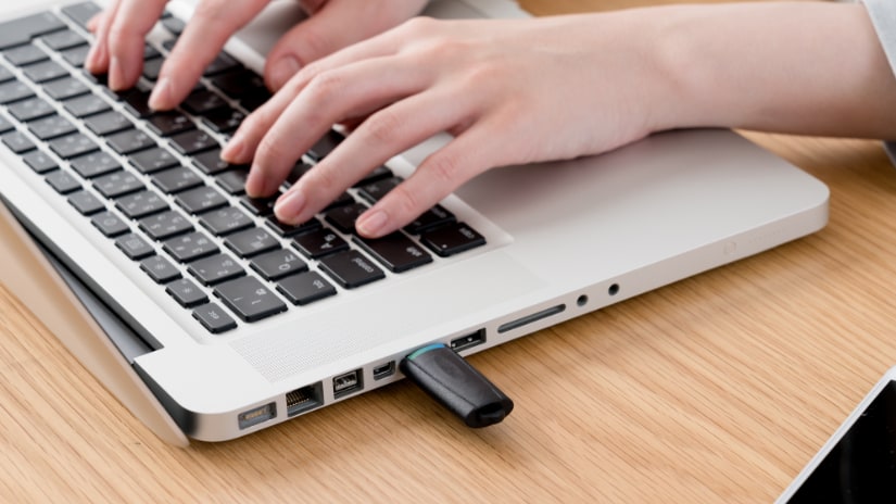 A laptop with an Internet dongle in the side and someone typing on the keyboard